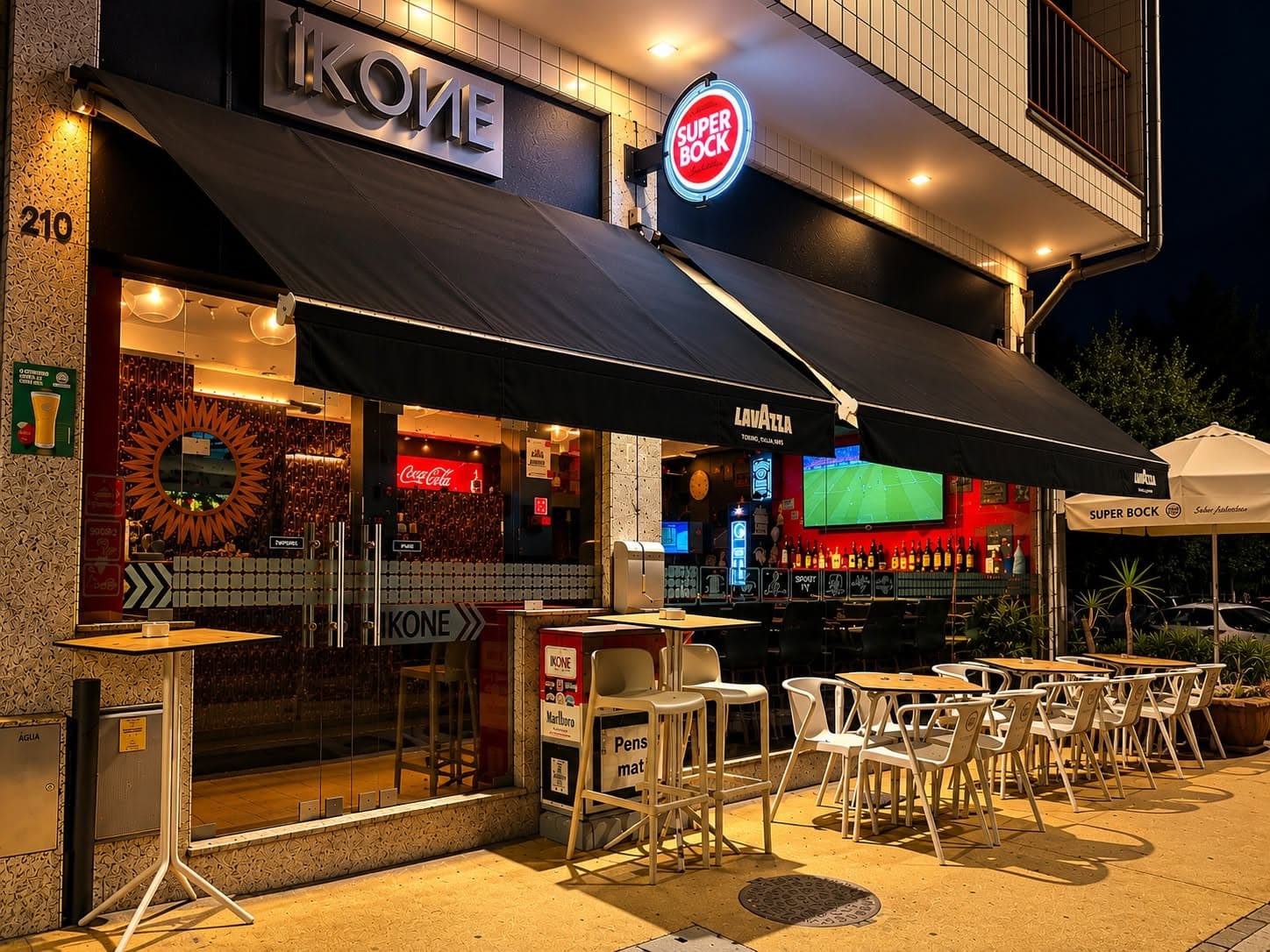 Fachada do IKONE bar à noite, com toldos pretos e esplanada